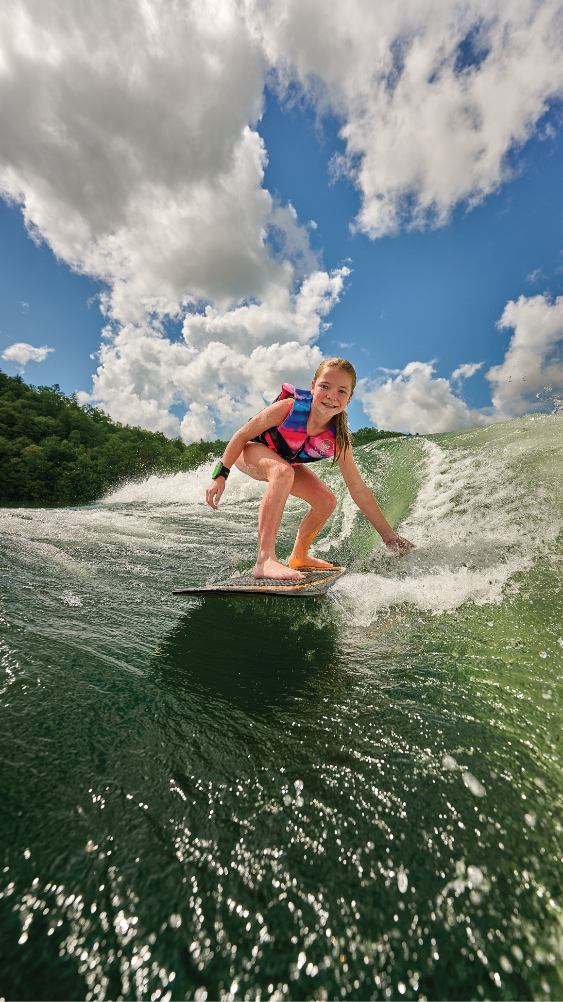 Young surfer in a life vest carving the wake behind a boat