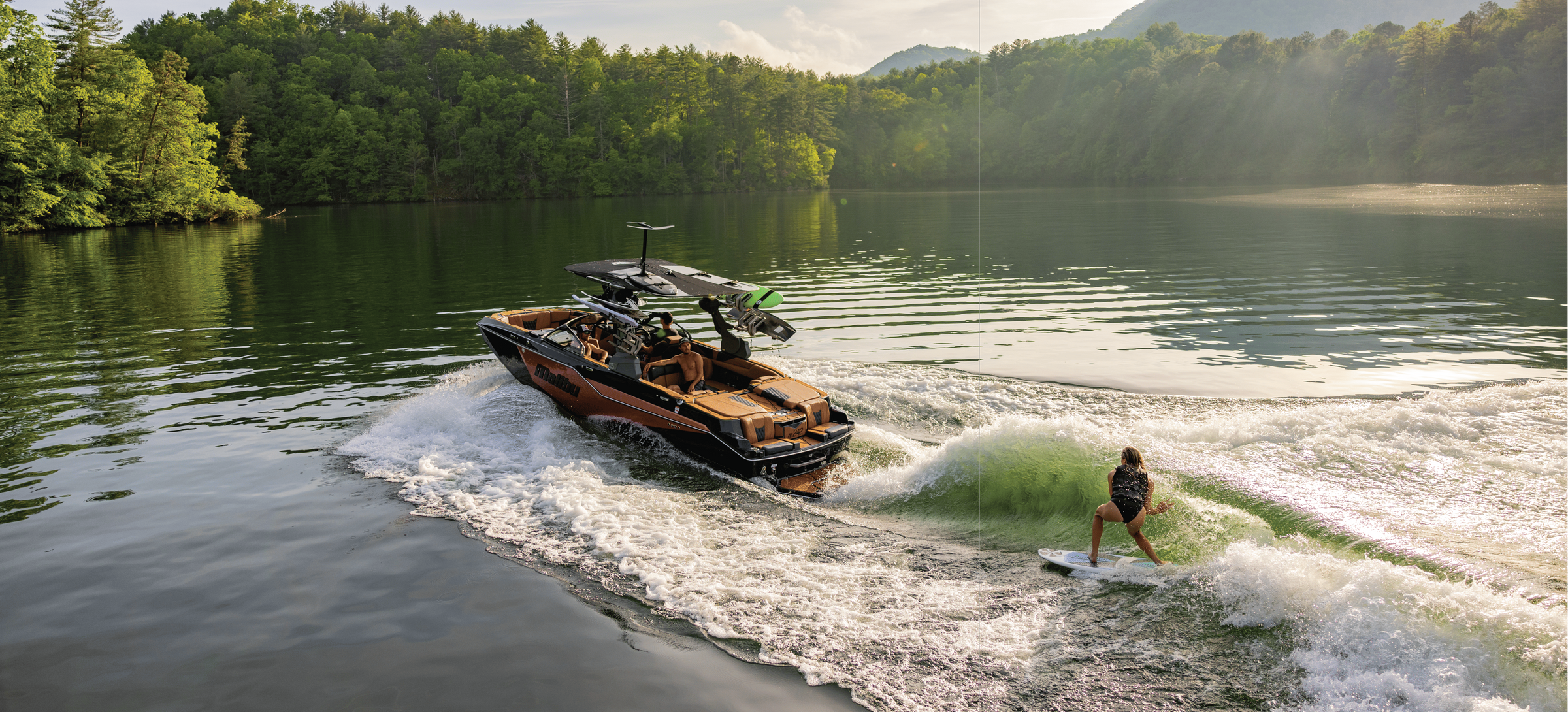 Aerial view of a camo-wrapped Malibu wakeboat with a surfer on the wave