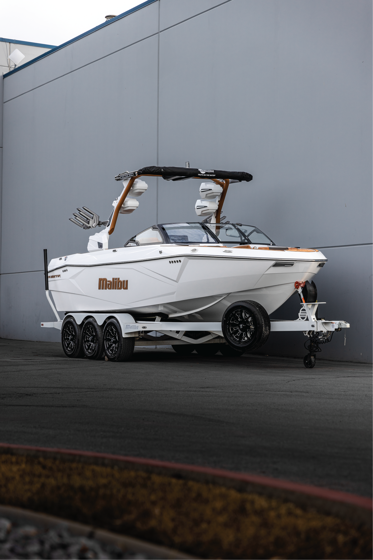 White Malibu wakeboat on a triple-axle trailer parked outside