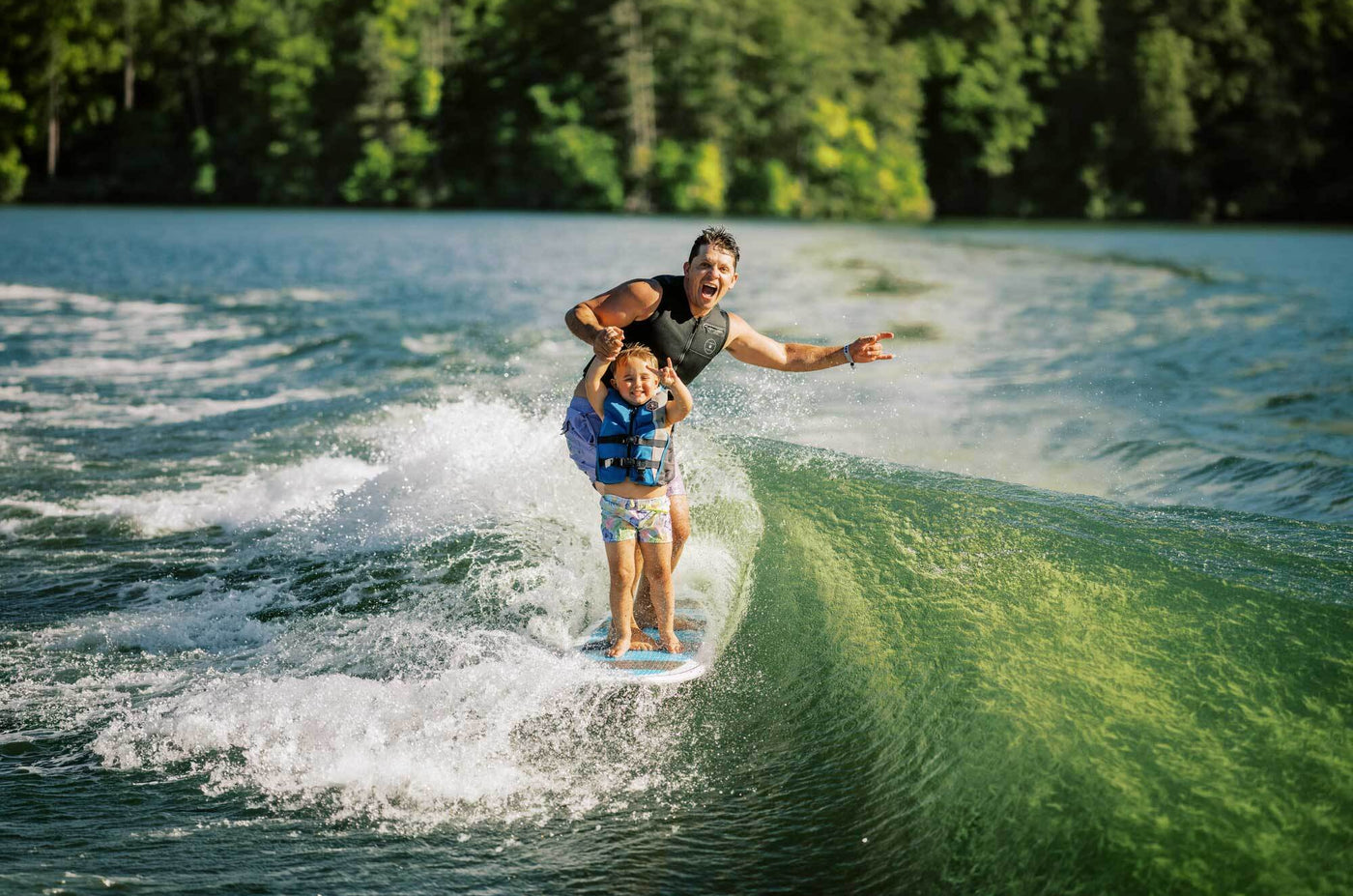 Man and child wakeboarding on a lake with trees in the background