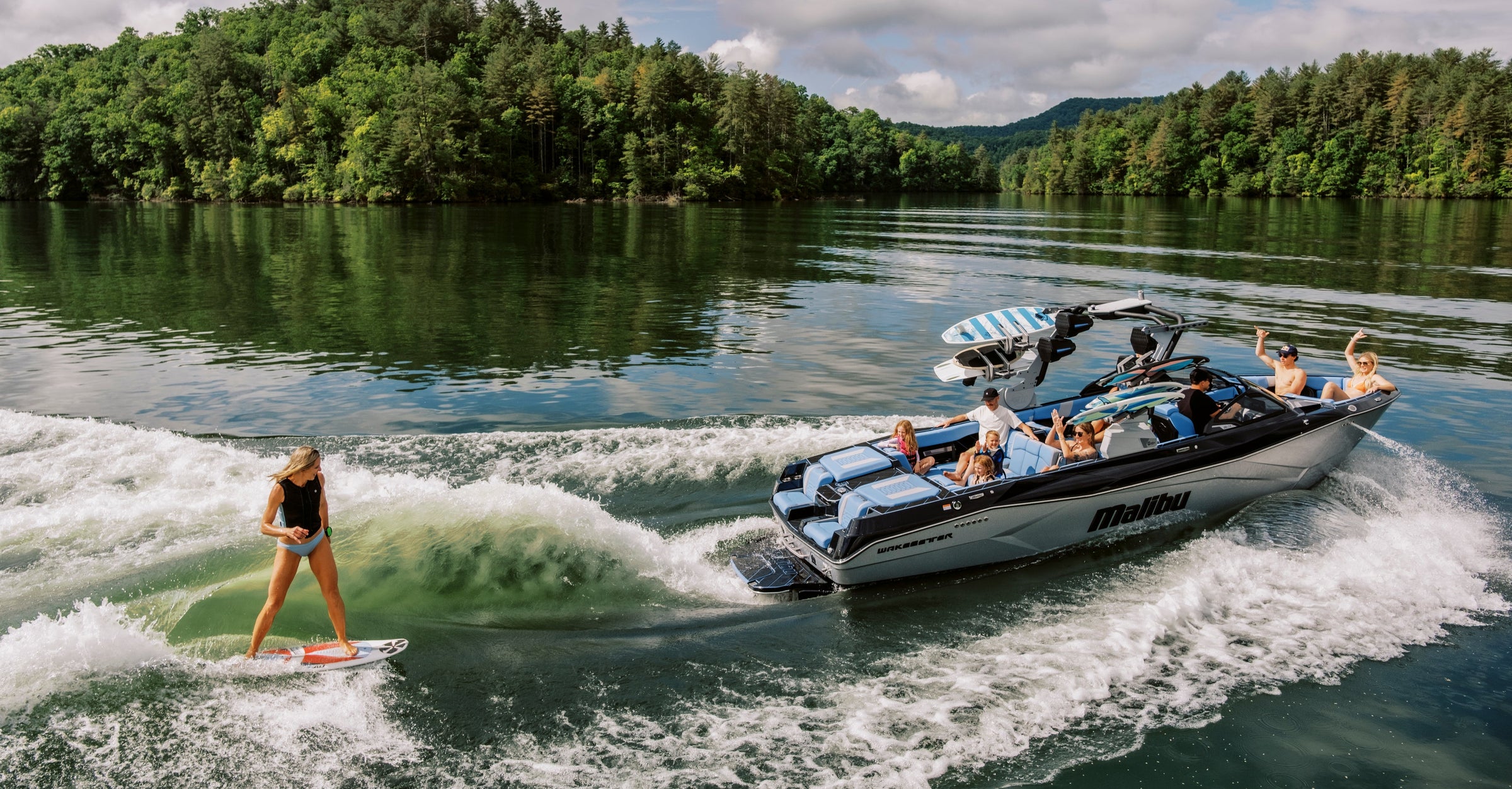 Wakesurfer riding the wave behind a Malibu wakeboard boat on a green lake