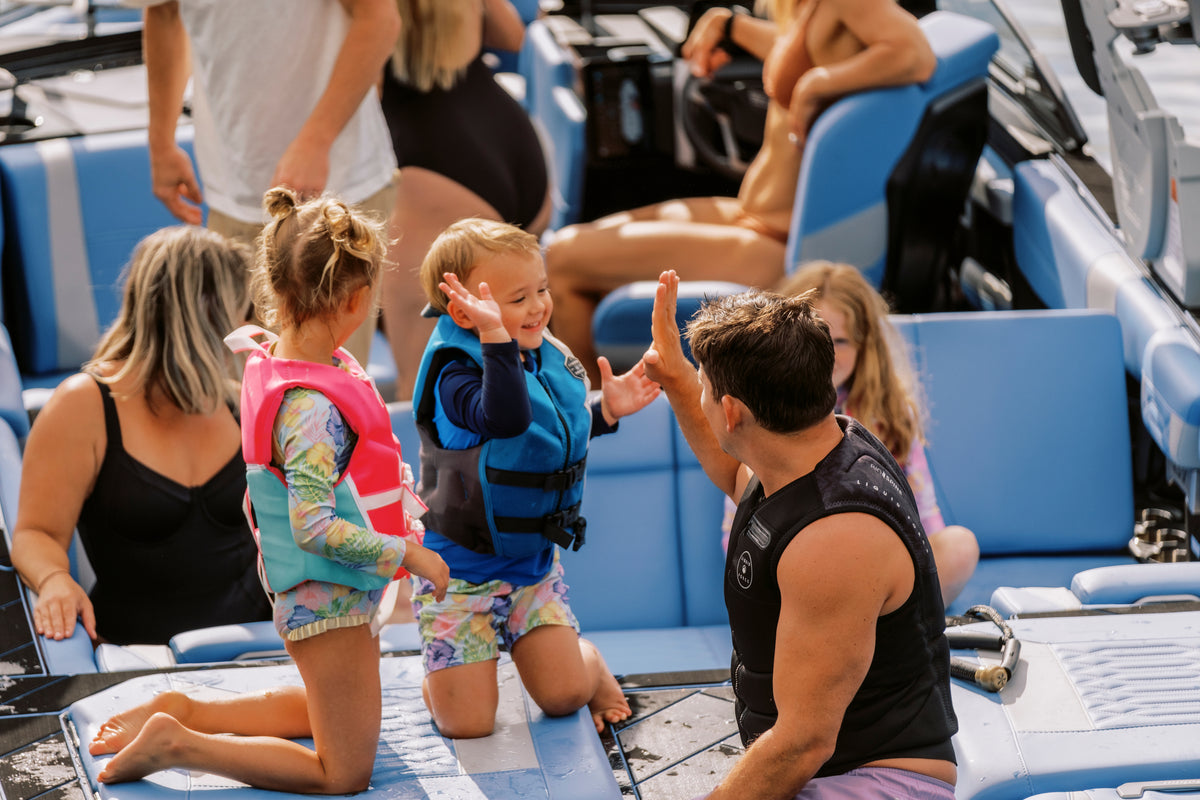 Adult giving a young child a high five on the back of a wakeboard boat