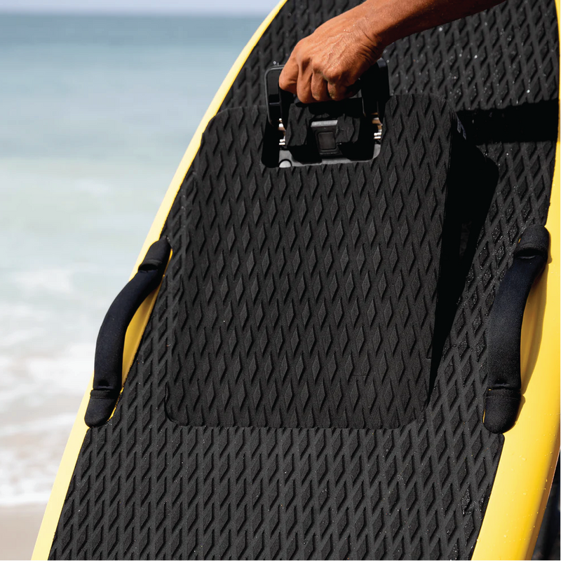 Hand gripping the carry handle on a black e-foil board deck at the beach