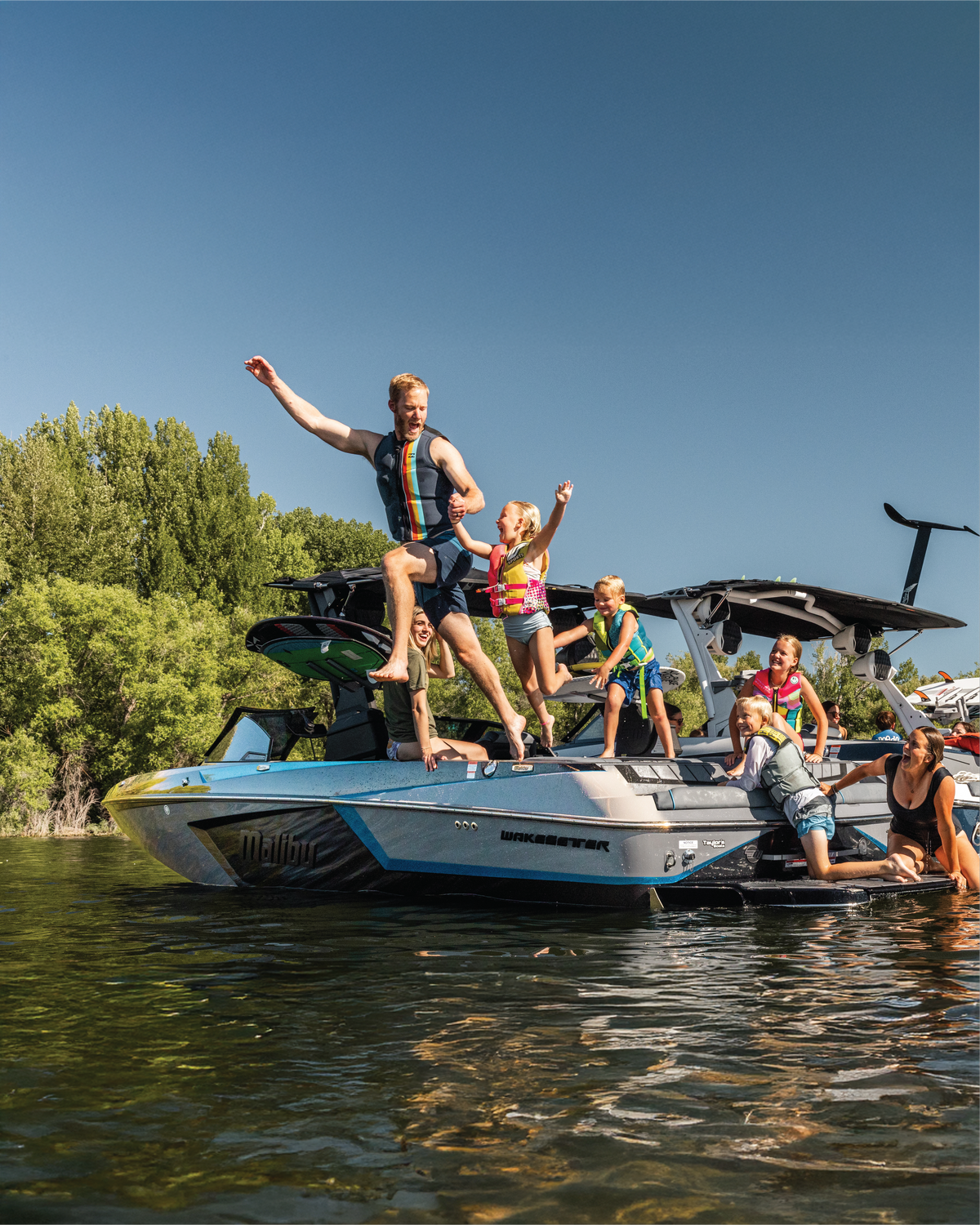 People enjoying a day on a boat with a clear blue sky and green trees in the background.