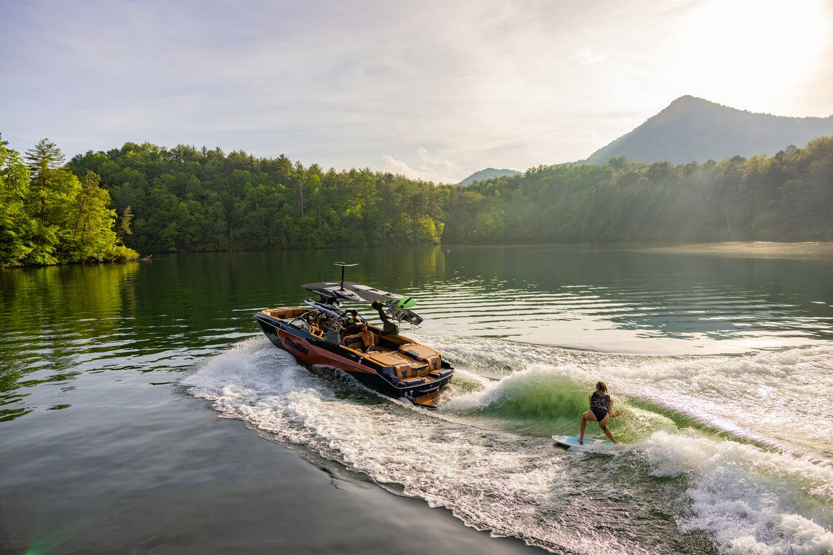 Wakesurfer riding behind a Malibu boat on a lake with a mountain backdrop