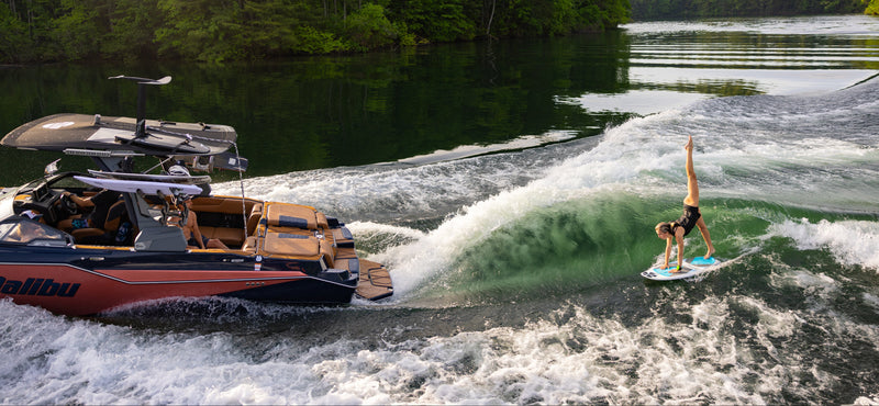 Wakesurfer riding a clean wave behind a red Malibu boat on a river