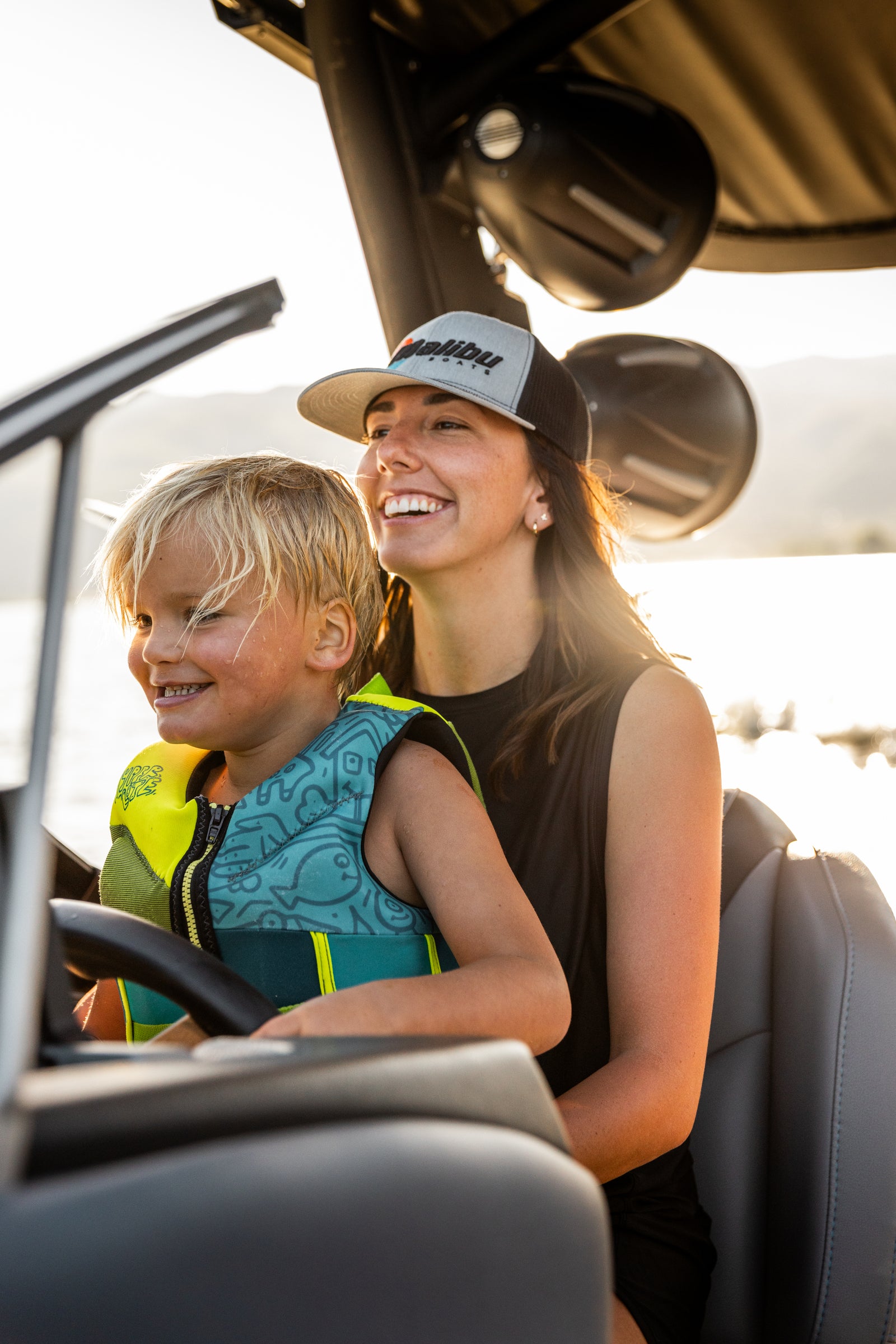 Smiling woman in a Malibu hat and child in a life vest at a boat's helm