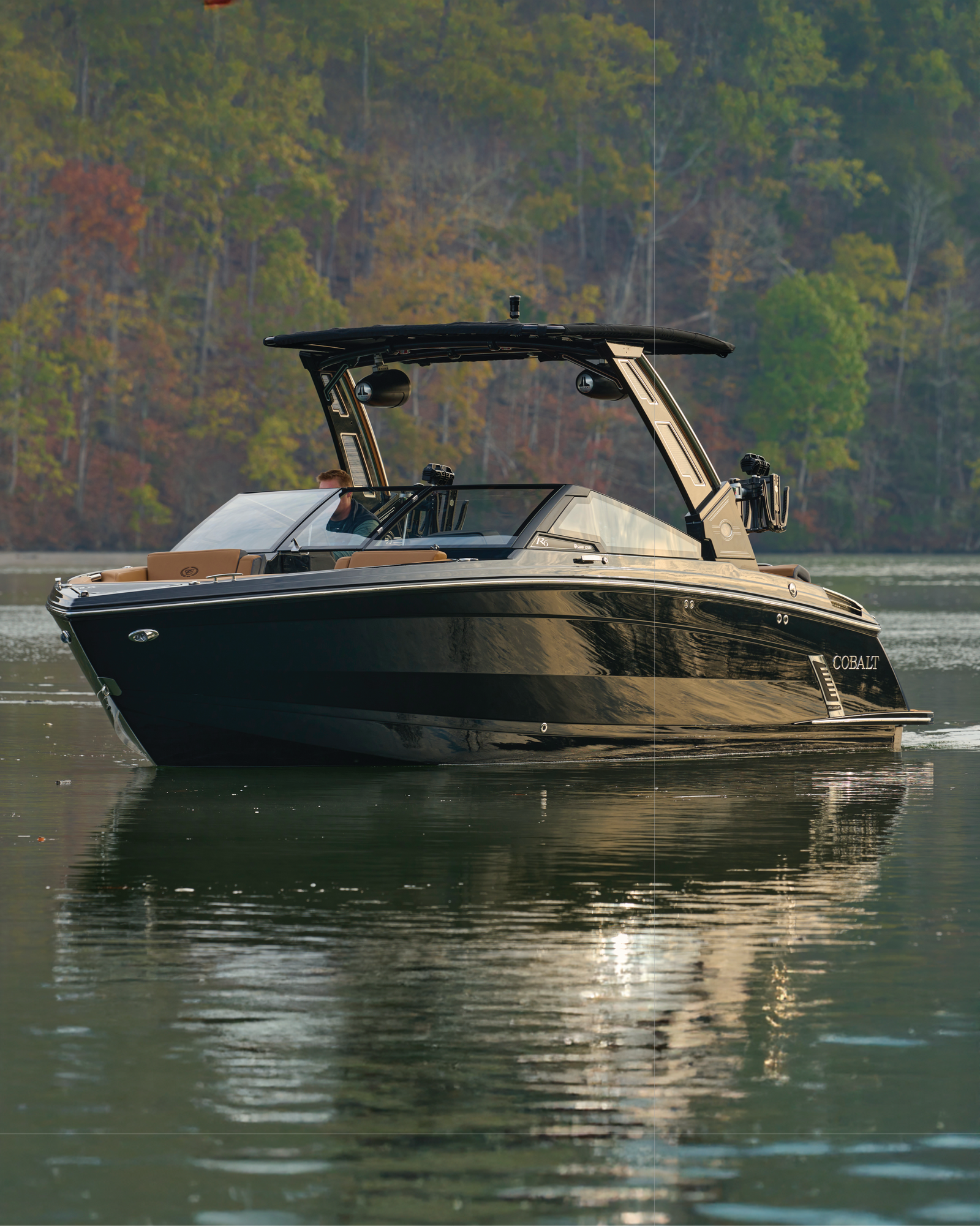 Black Cobalt bowrider boat on a calm lake with autumn foliage behind