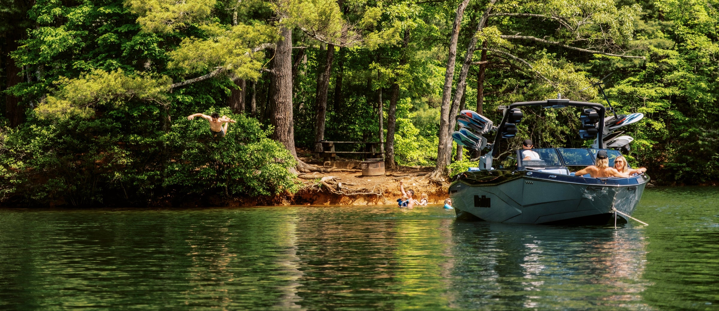Blue Malibu boat anchored near a wooded shoreline on a calm lake
